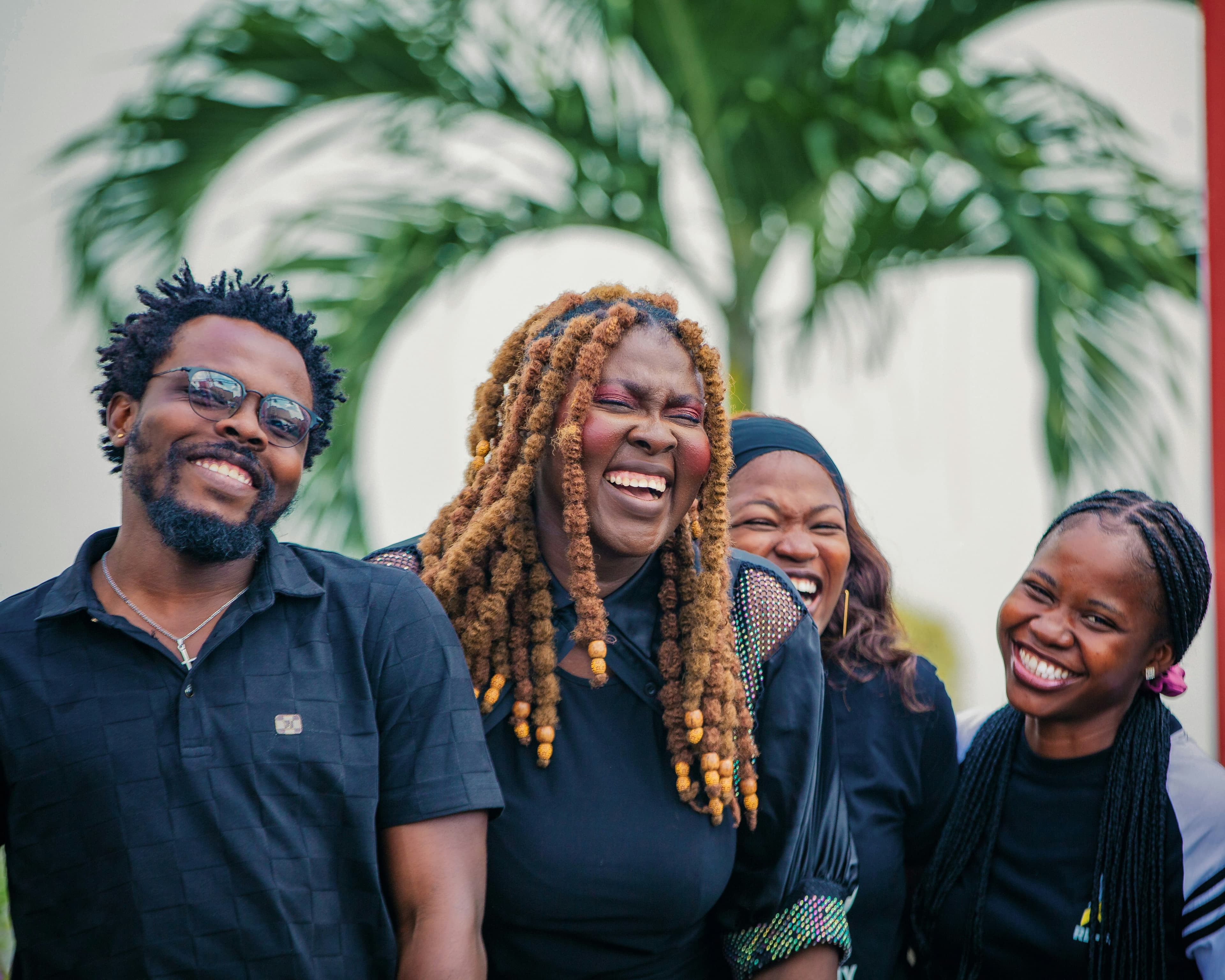 Four young professionals in dark shirts laughing together outdoors in front of a palm tree